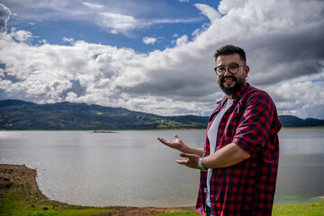 Latino man wearing oversized glasses posing from a viewing platform with Lake Guatavita in the...