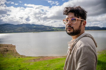 Latino man wearing oversized glasses posing from a viewing platform with Lake Guatavita in the...