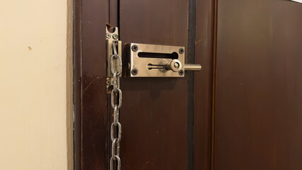A close-up of a dark wooden door secured with a metal slide bolt and a hanging chain latch, both...