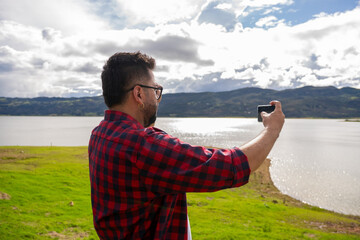 Hipster Latino man in a red striped shirt using his phone by Lake Guatavita. Concepts of...