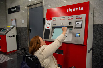 Woman in wheelchair buying subway ticket at ticket machine. Concept of inclusion, adapted public