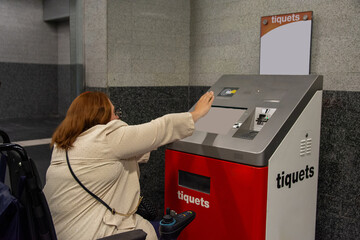 Woman in wheelchair using ticket machine in subway station. Concept of inclusion, adapted public