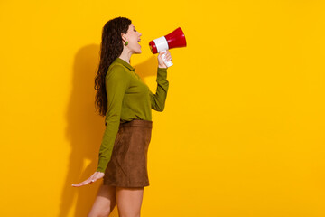 Brunette young woman with megaphone promoting communication in vibrant yellow background in casual...