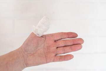 Bandaged left thumb against a light wall. Injuries and first aid