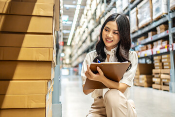 Focused on her task, young asian woman sitting and holding clipboard meticulously updates inventory records while surrounded by shelves filled with various products in a vibrant warehouse setting