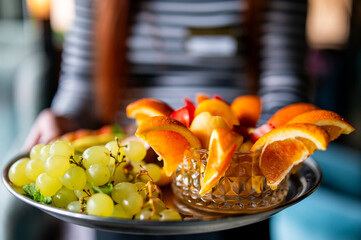 Close-up of fresh green grapes and orange slices served on a tray, held by a person in a striped shirt. Healthy snack presentation with vibrant natural colors.