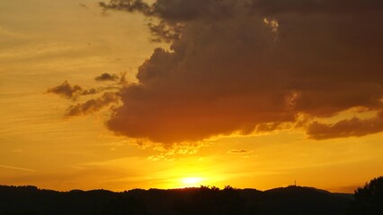 Dramatic sunset sky over forest hills with glowing orange clouds