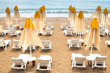 Beach scene with empty closed umbrellas and sun loungers on on sea shore