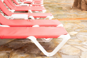 A row of pink deck chairs standing near hotel swimming pool.