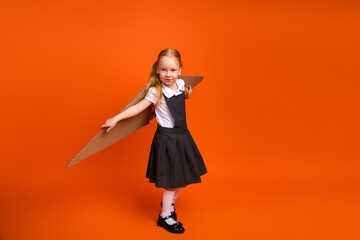Adorable young girl in uniform with cardboard airplane prop on vibrant orange background...