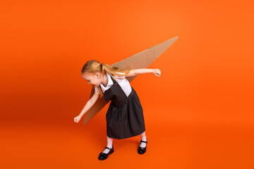Young excited girl in a school uniform posing in front of an orange background with a cardboard...