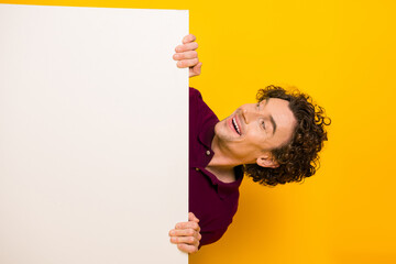Cheerful young man in burgundy polo holding blank whiteboard on vibrant yellow background