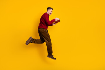 Young Positive Man Reading Book While Jumping Against Yellow Background in Trendy Clothing