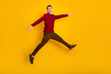Cheerful Young Man Jumping Against Bright Yellow Background Wearing Stylish Red Sweater
