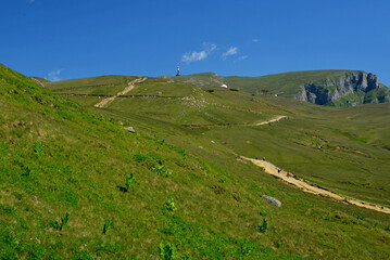 Obraz premium Green waving hills of the Carpathian Mountains in the Bucegi area and hikers heading to the Caraiman Cross