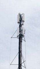 Tall cellular communication tower with multiple antennas and equipment mounted on metal framework against overcast sky. Telecommunications infrastructure for mobile networks and data transmission.
