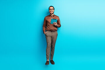 Confident Young Professional Holding Digital Tablet Against Vibrant Teal Background Showcasing...