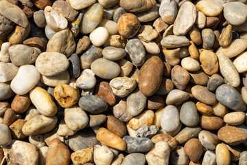 Top view of a collection of smooth, multicolored river pebbles lying on the ground. 