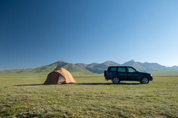 Landscape with SUV car truck and set up tents at a camping site by a highland freshwater lake surrounded by high mountains. Song Kul Lake, Kyrgyzstan, Central Asia. Road trip, travel camping concept.