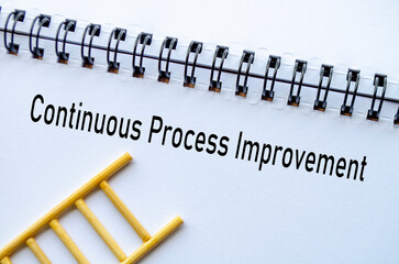 Continuous Improvement on notebook with ladder on wooden background