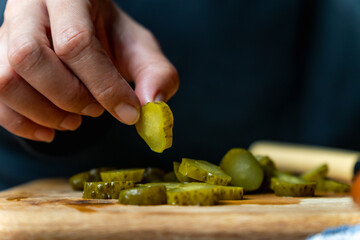 A person is cutting up pickles into thin slice on a wooden cutting board