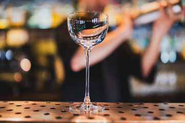 Empty cocktail glass on a modern metal bar counter with blurred bartender in background. Elegant scene capturing preparation in upscale bar environment.
