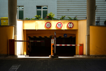 Parking garage entrance. Yellow facade. Multiple traffic signs. Barrier gate closed.

