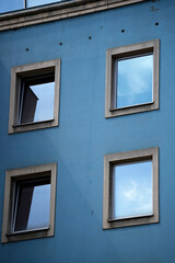 Blue building facade. Square windows. Reflective glass. Urban exterior.

