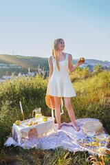 Summer picnic in nature with stylish woman holding hat and lemonade in golden light.