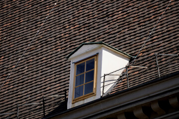 Traditional attic window with wooden frame set in steep tiled roof. Classic architectural detail of European buildings emphasizing craftsmanship, texture, and timeless design.

