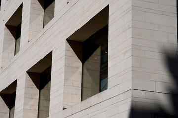 Modern minimalist building with geometric square windows and textured stone facade under deep blue sky. Sharp lines and shadows emphasize architectural precision and urban elegance.


