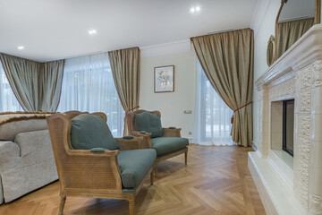 The elegant living room is decorated in a modern style with luxurious sofas and a fireplace. Natural light penetrates through the large windows, creating a warm atmosphere.