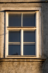 Old window with wooden frame on a weathered stone wall illuminated by warm evening sunlight. Vintage architectural element with textured surface and nostalgic charm.