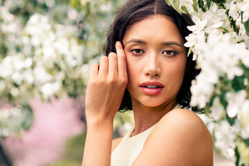 Beautiful young woman surrounded by springtime blossoms in a serene outdoor setting featuring...