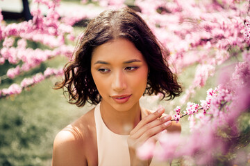 Gorgeous woman enjoying a sunny day in a blooming garden surrounded by vibrant pink blossoms,...