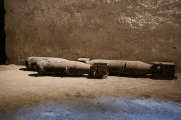 Weathered unexploded WWII bombs lying on dusty ground against textured concrete wall. Historical military ordnance creates powerful wartime atmosphere.
