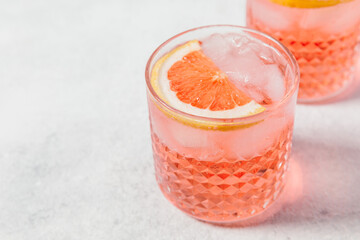 A refreshing pink paloma cocktail with ice cubes, topped with a slice of grapefruit, served in a...