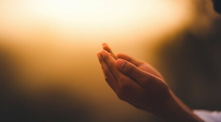 Man's cupped hands in prayer against a bokeh golden sunlight background.