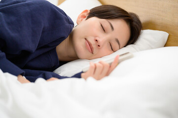 スマートフォンを手にしたまま微笑みながら眠りにつく女性の寝顔