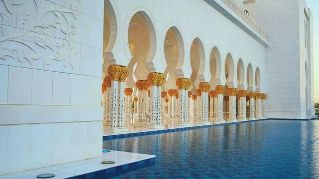 Beautiful fabulous building Arabian attraction. White wall decorated marble carvings, columns gold, floral patterns. Muslim temple reflected in blue water. Beauty oriental architecture. No people. UAE