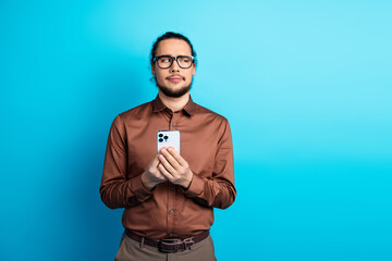 Young businessman holding a smartphone in a casual and stylish brown shirt against a bold teal...