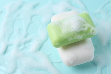 Soap bars with foam on light blue background, above view. Space for text