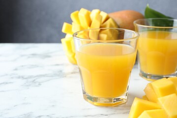 Tasty mango juice in glasses and fresh fruits on white marble table, closeup. Space for text