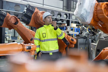 Asian worker uses a walkie talkie near robotic arms in a modern factory
