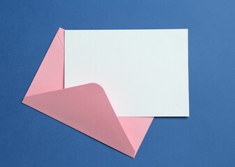 Blank invitation card and envelope on blue background, top view. Space for design