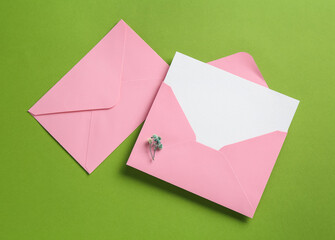 Blank invitation card and envelopes on green background, flat lay. Space for design