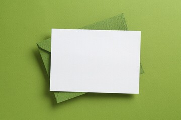 Blank invitation card and envelope on green background, top view. Space for design