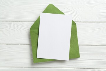 Blank invitation card and envelope on white wooden table, top view. Space for design