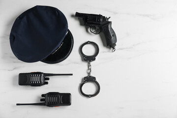 Police cap, gun, handcuffs and walkie talkie on white marble table, flat lay. Space for text