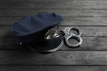 Police cap and handcuffs on black wooden table, closeup